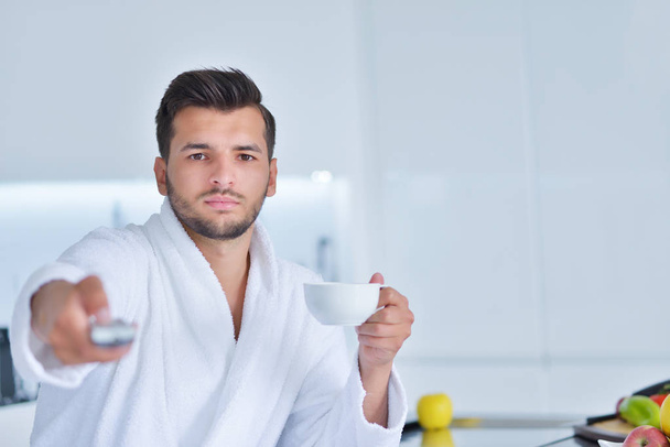 Young man in bathrobe sitting on kitchen  - Valokuva, kuva