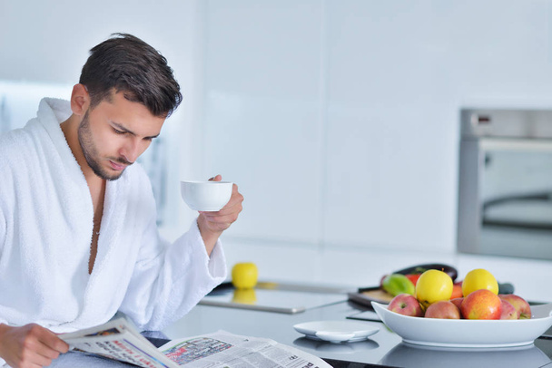 Young man in bathrobe sitting on kitchen  - Foto, immagini