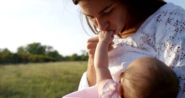 Super slow motion of young caucasian mother kissing tenderly her baby girl in a meadow of vineyard on a sunshine in 4k (close up with flares) - Photo, Image