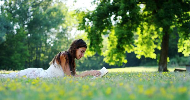 On a sunny day a beautiful woman relaxes in the shade of a tree to read a book and relax, the book really like the woman who is a lover of literature and silence. relax - Photo, Image