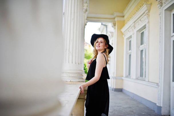 Blonde woman on black dress, necklaces and hat against vintage h - Fotografie, Obrázek
