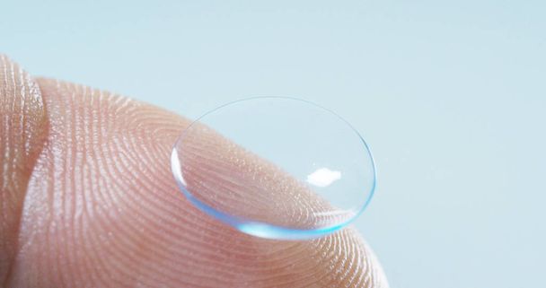 Macro shot of a finger holding a contact lens technology with a chip to see better in both eyes and increase diopters. Concept: eye examination, optical, immersive technology - 写真・画像