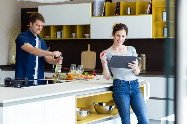 Handsome young man opening wine bottle while his wife using digital tablet in the kitchen. - Foto, Imagem
