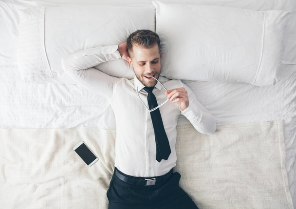 Top view. Handsome businessman with glasses lying on bed - Foto, Imagem