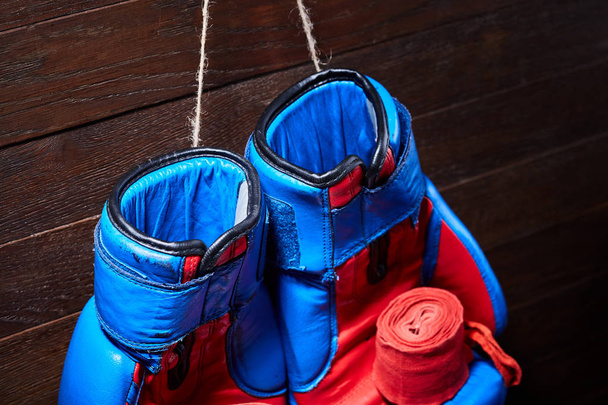 Blue and red boxing gloves and bandage on brown plank background. - Foto, Bild