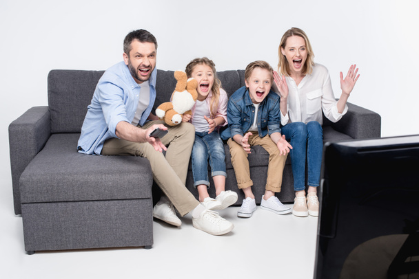 perhe katsomassa televisiota istuessaan sohvalla
 - Valokuva, kuva