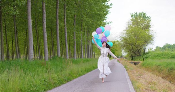 Beauty Girl with Healthy Long Hair Outdoors. Happy Smiling Young Woman Enjoying Nature. Beautiful Young Woman having Fun with balloons in the Meadow. Freedom concept. Sunset - Foto, Imagem