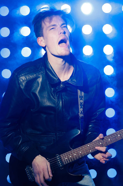 jovem músico de rock tocando guitarra elétrica e cantando. Estrela de rock no fundo dos holofotes
 - Foto, Imagem