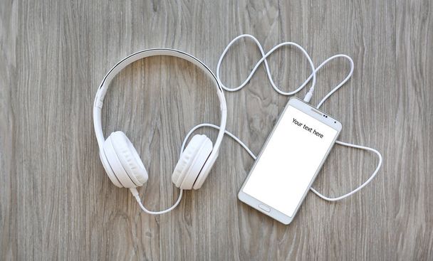 headphones and smartphone with word "Your text here" on white screen against wooden background - Photo, image