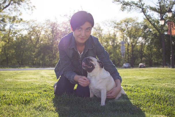 portrait of young woman and pug having god time in the park on green grass during sunset or sunrise  - Φωτογραφία, εικόνα