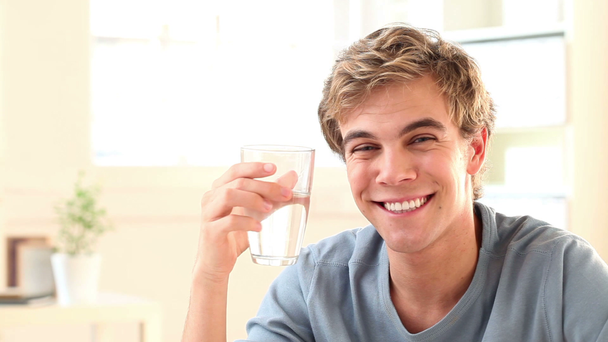 Gesunder junger Student trinkt ein Glas Wasser, während er zu Hause in seinem Arbeitszimmer studiert - Filmmaterial, Video