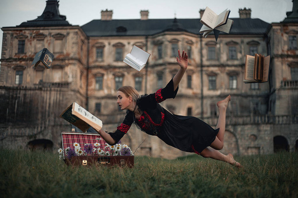 Femme sorcière lit livre et vole dans l'air sur fond d'ancien château. Lévitation
.  - Photo, image