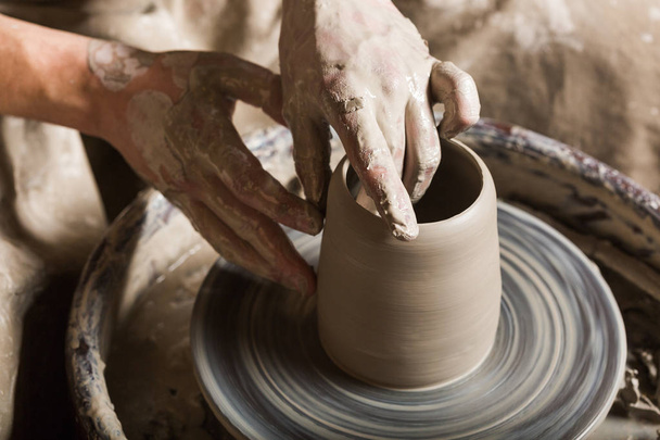 pottery, workshop, ceramics art concept - close up on male hands sculpt some new utensil with fingers and water, man hands works with potters wheel and raw fireclay, top view. - Фото, изображение