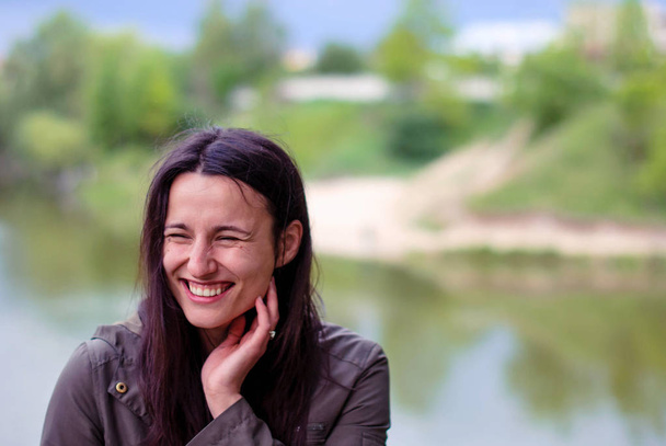 A beautiful girl without makeup with long dark hair laughing near the river. - Photo, Image