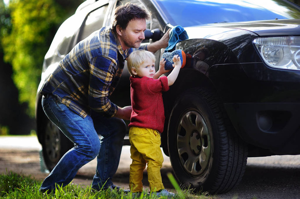 Middle age father with his toddler son washing car together outdoors - Foto, Imagen