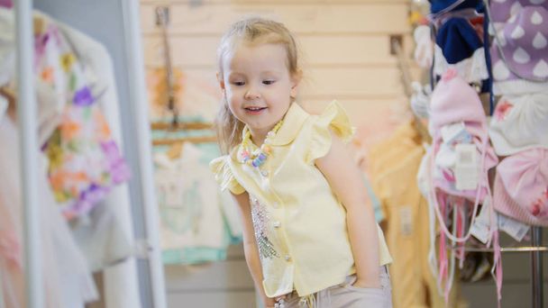 Cute girl looking at herself in the mirror in the childrens clothing store - Foto, Imagen