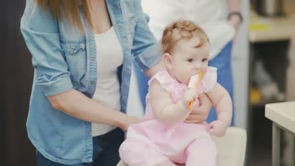 A half-year-old baby in a pink dress scratches her gum. Baby with mom - Felvétel, videó