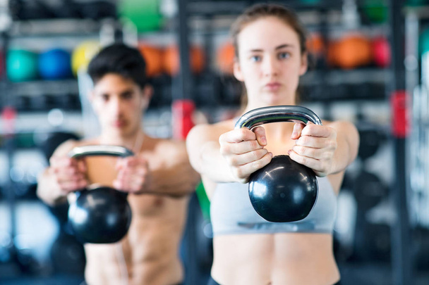 Young fit couple in gym exercising with kettlebell. - Zdjęcie, obraz
