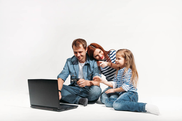 Szczęśliwa Rodzina ojciec, matka i dziecko, leżąc na podłodze z laptopa i karty kredytowej na na białym tle - Zdjęcie, obraz