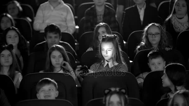 Black and white picture. Little beautiful girl looks at himself in the hall cinema. Many children sitting. - Footage, Video