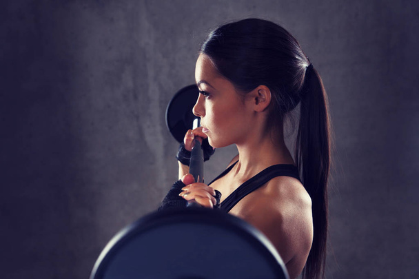 young woman flexing muscles with barbell in gym - Foto, Bild