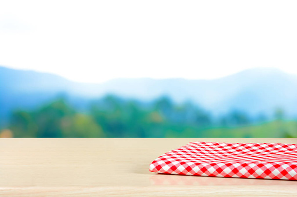 Punainen ruudullinen kangas puupöydällä hämärän vuoren taustalla
 - Valokuva, kuva