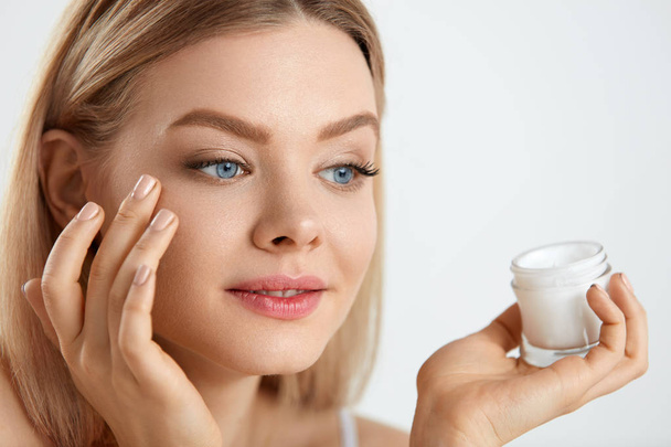 Beauty Woman Face. Girl With Fresh Skin And Cream Bottle In Hand - Фото, изображение