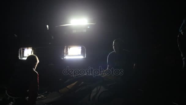 Ночная съемка двух взрослых мужчин и ребенка, устанавливающих палатку в свете внедорожника
. - Кадры, видео