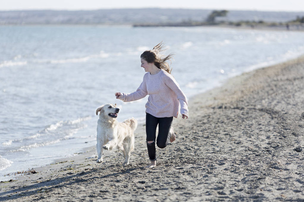 Tienermeisje spelen met haar hond op een strand.  - Foto, afbeelding