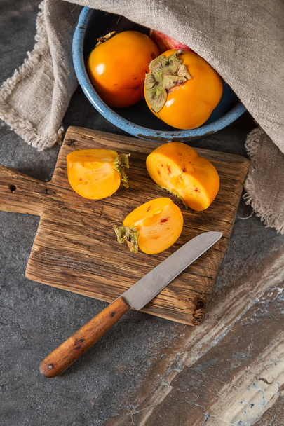Ripe orange persimmon in a blue bowl on a wooden tray. Diet, or  - 写真・画像