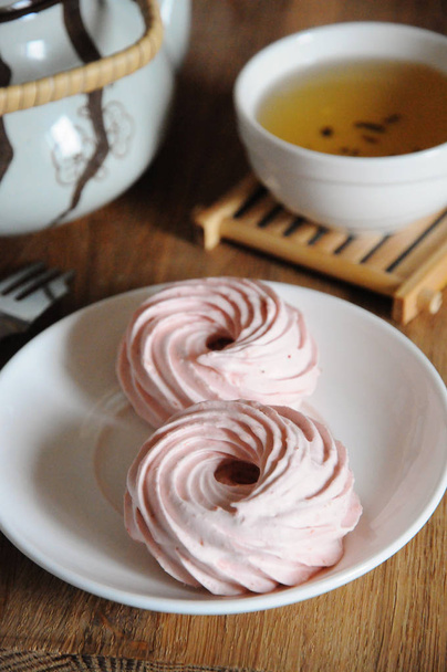 Marshmallow alla fragola naturale su piattino bianco, forchetta da dessert, bollitore e ciotola con tè verde
 - Foto, immagini