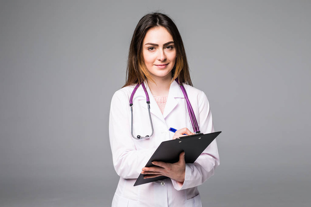Portrait of happy pretty young woman doctor with clipboard and stethoscope over grey background - Foto, imagen
