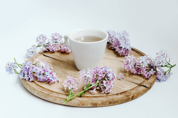 Φλιτζάνι τσαγιού με λιλά ανοιξιάτικα λουλούδια πάνω στο ξύλινο τραπέζι. Λευκό φόντο - Φωτογραφία, εικόνα