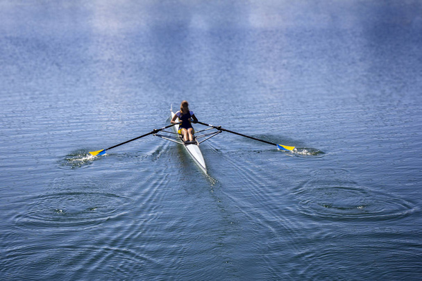 Молода жінка веслує в човні на озері
 - Фото, зображення