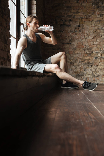 Portrait of a tired sportsman drinking water from a bottle - Photo, Image