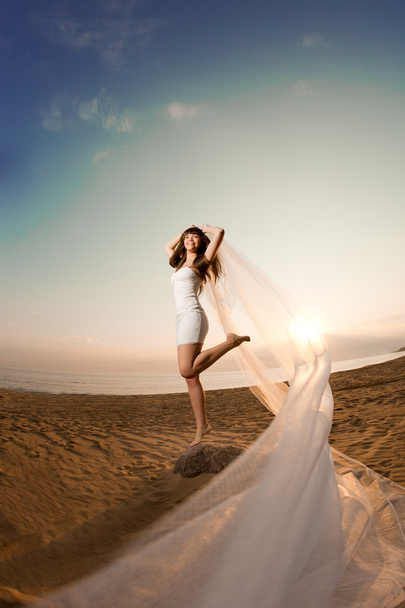 Beautiful bride with a long veil on the beach at sunset - Fotó, kép