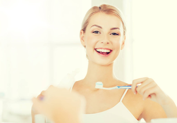 woman with toothbrush cleaning teeth at bathroom - Foto, Bild