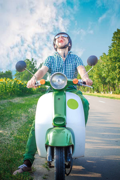 Chico alegre se ríe fervientemente montando un scooter retro
 - Foto, Imagen