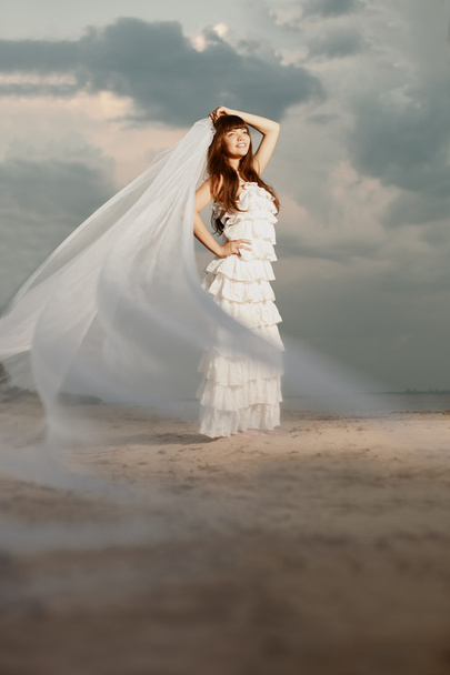 Beautiful bride with a long veil on the beach at sunset - Foto, Imagem