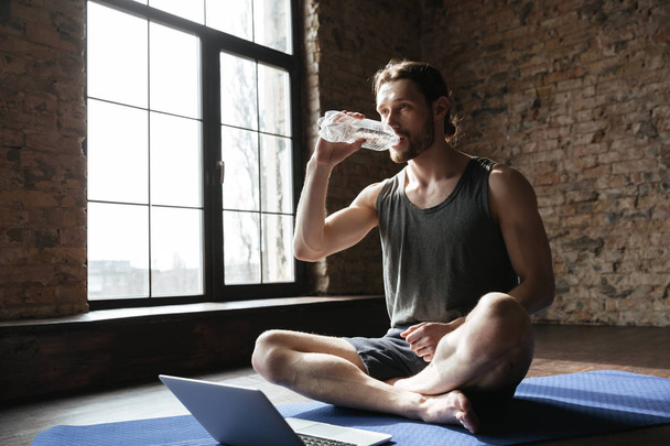 Sportsman in gym sitting on floor drinking water - Photo, Image