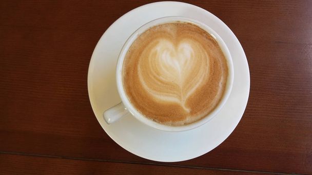 Bílý hrnek s kávou a mlékem s výkresy v podobě srdce na dřevěné pozadí - Fotografie, Obrázek
