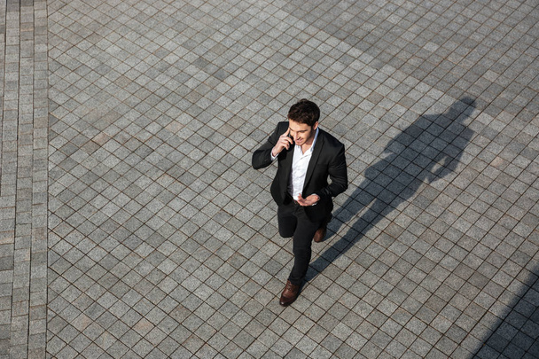 Happy young businessman walking outdoors - 写真・画像