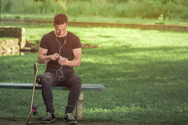 Skater sitting on bench in the park and using smartphone - Valokuva, kuva