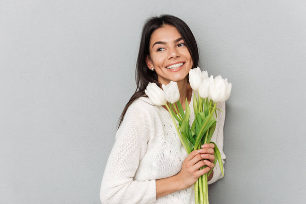 Cheerful woman standing over grey wall with flowers - Foto, Imagen