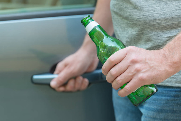 Mies avaa autonsa pitelemällä kaljapulloa
 - Valokuva, kuva