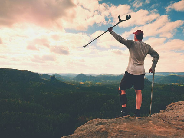 Wanderhütten Knie. Mann mit Bein in Wegfahrsperre bleibt auf Gipfel und hebt Medizin über Kopf. - Foto, Bild