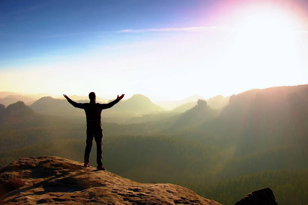 Randonneur en noir. Un geste de triomphe. Grand touriste sur le sommet du rocher de grès dans le parc national Saxe Suisse regarder dans le paysage brumeux
. - Photo, image