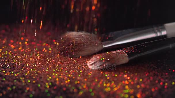 Red sparkles falling on makeup brushes on the black background, abstract slow motion - Πλάνα, βίντεο