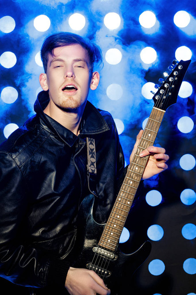 jeune musicien rock attrayant jouant de la guitare électrique et chantant. Rock star sur fond de projecteurs
 - Photo, image