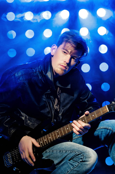 young attractive rock musician playing electric guitar and singing. Rock star on background of spotlights - Foto, afbeelding